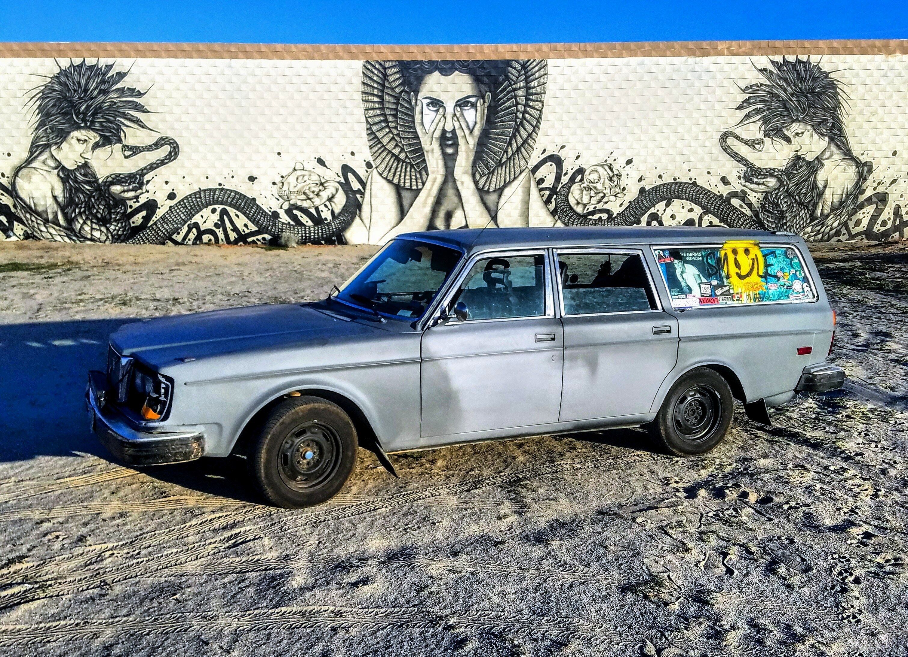 A silver station wagon parked in front of a mural with a woman and snakes.