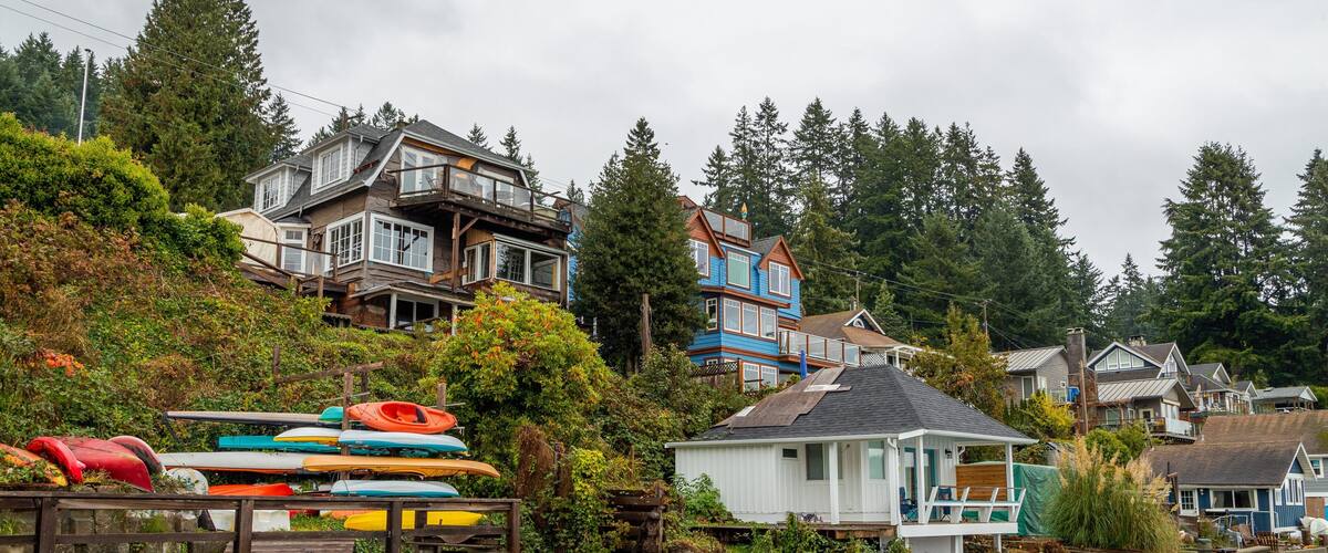 A waterfront with houses, kayaks, and a small dock.