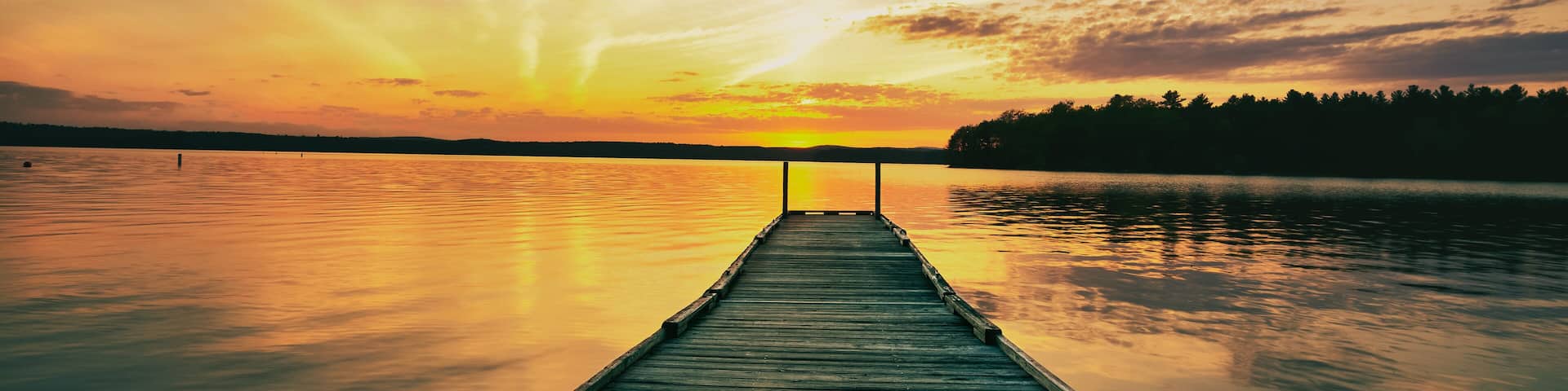summer sunset over the lake looking at the fishing dock and the forest on the horizon