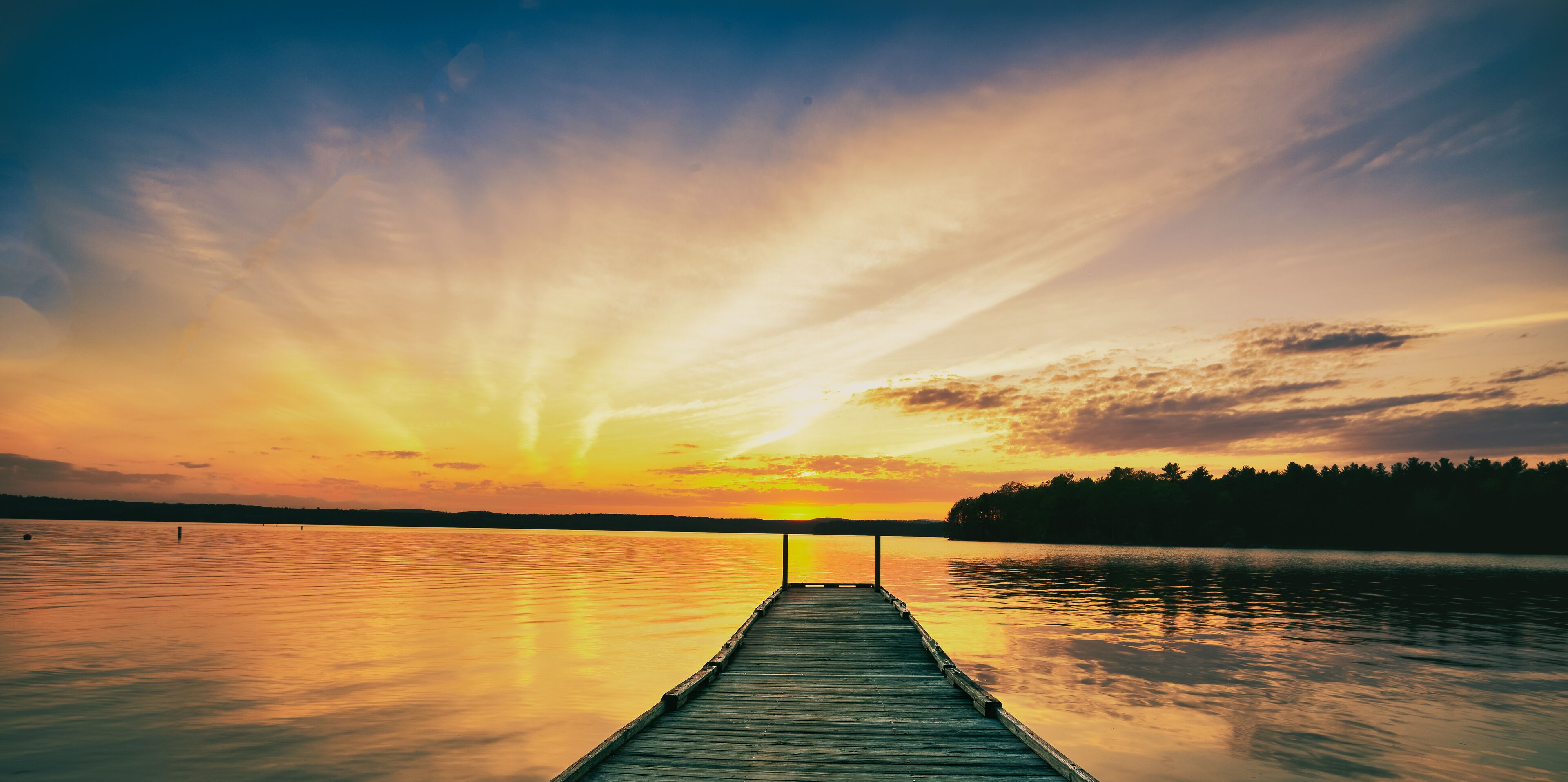 A wooden pier extending into calm water with a sunset in the background.