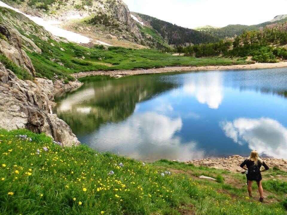 A calm lake surrounded by green hills and a rocky cliff.