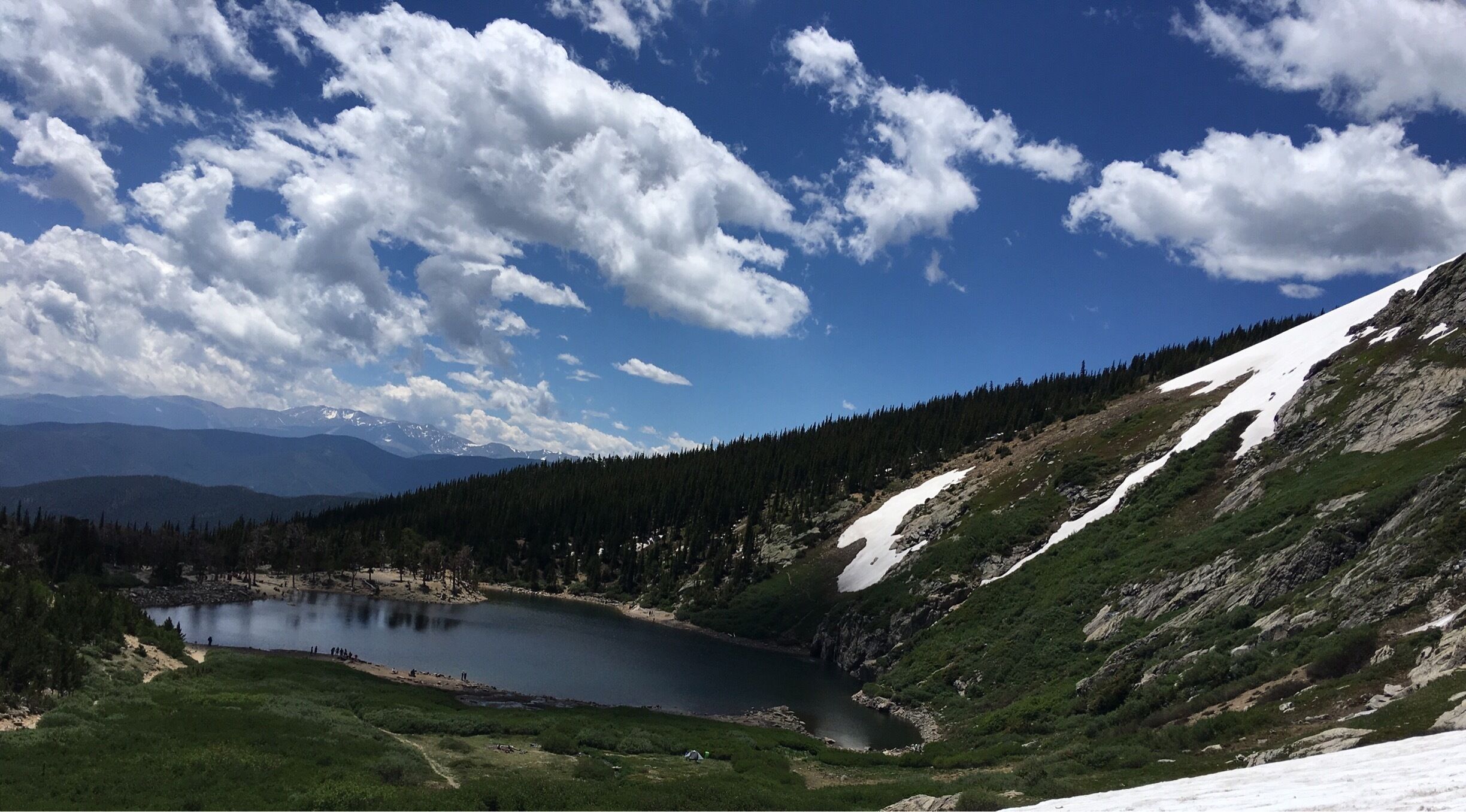 A mountain lake surrounded by forest and snow-covered slopes.