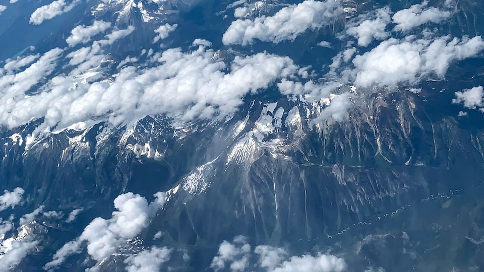 A mountain range with snow-capped peaks and scattered clouds.
