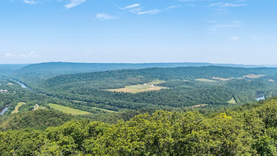 A valley with a river, surrounded by forested hills and a clear sky.
