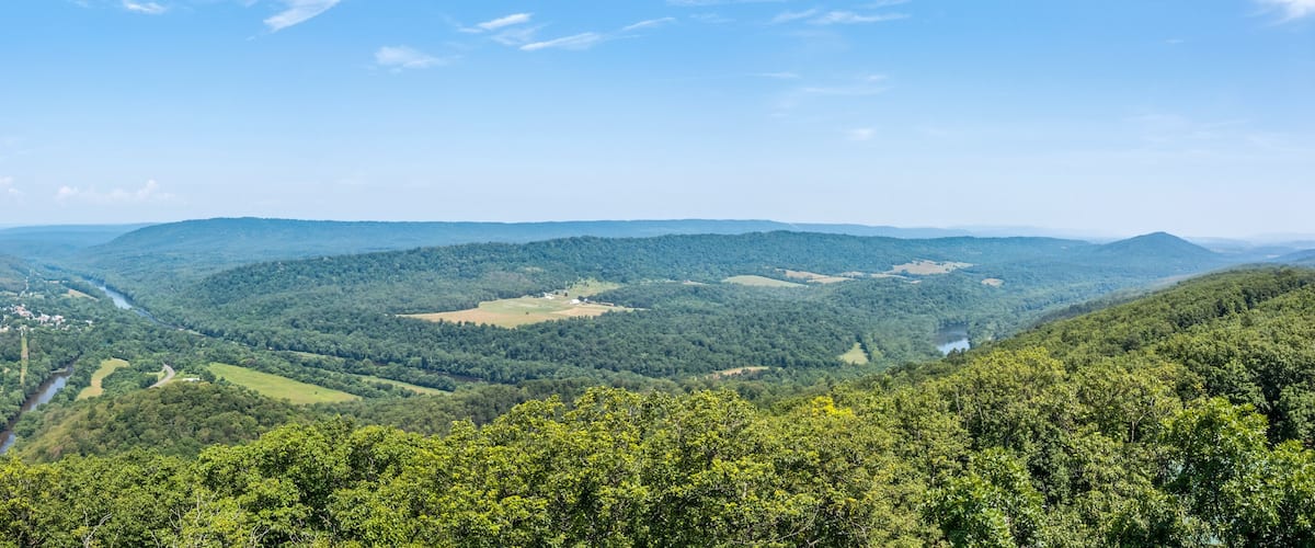 A valley with a river, surrounded by forested hills and a clear sky.