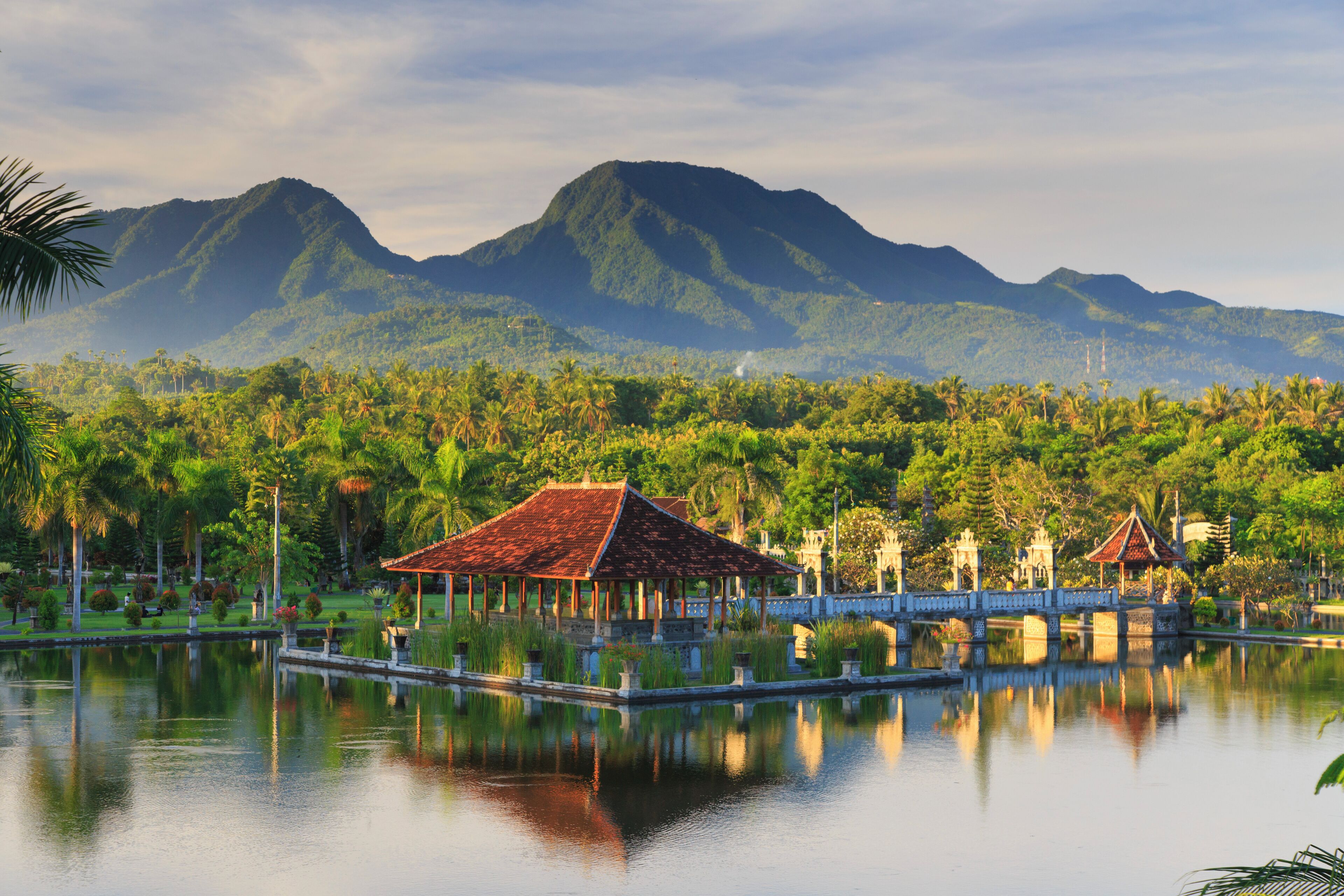 A serene lake with a traditional pavilion, lush greenery, and mountains in the background.