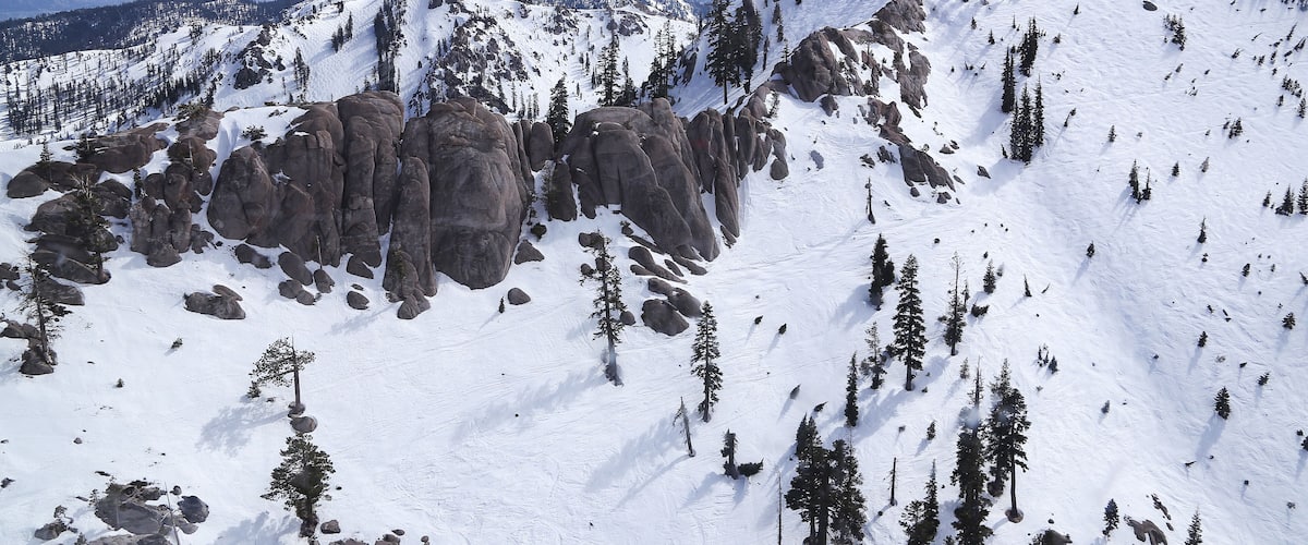 A snow-covered mountain with rocky outcrops and scattered trees.
