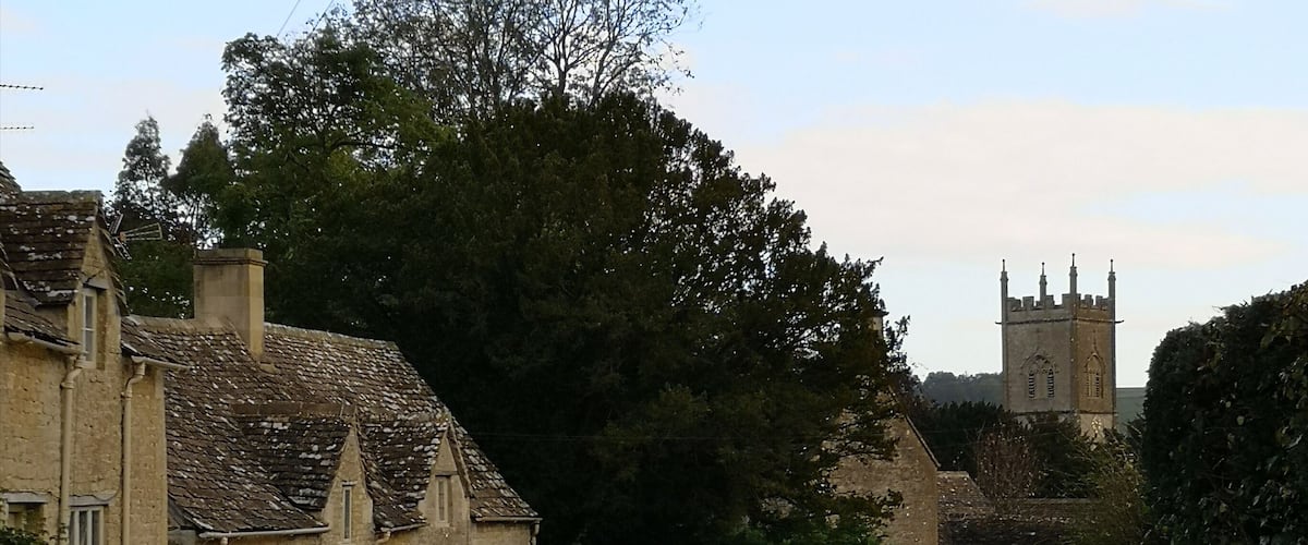 A rural road with stone houses, a school warning sign, and a church tower in the distance.