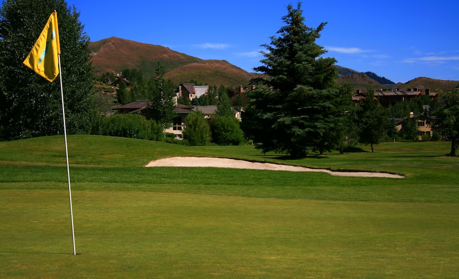 Un campo de golf con una bandera, búnkeres de arena y casas al fondo.