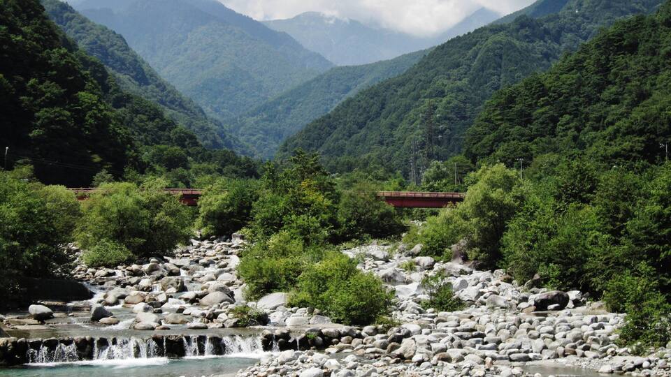 A river flowing through a mountainous landscape with a bridge in the distance.