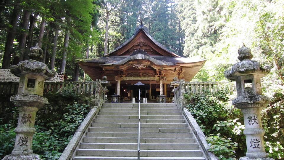 A traditional Japanese temple with a wooden structure, stone lanterns, and a staircase leading up to it.