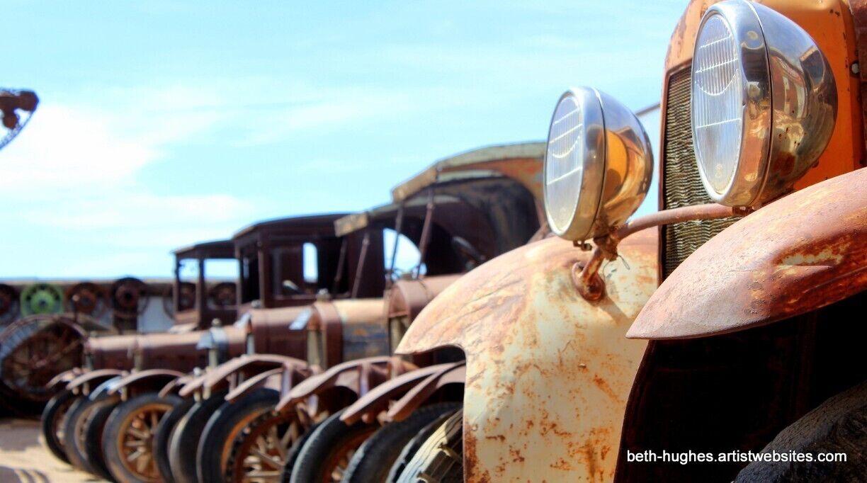 A row of rusted vintage car wheels and headlights.