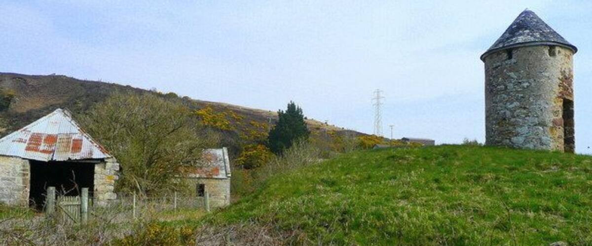 A stone tower and a small building on a grassy hill.
