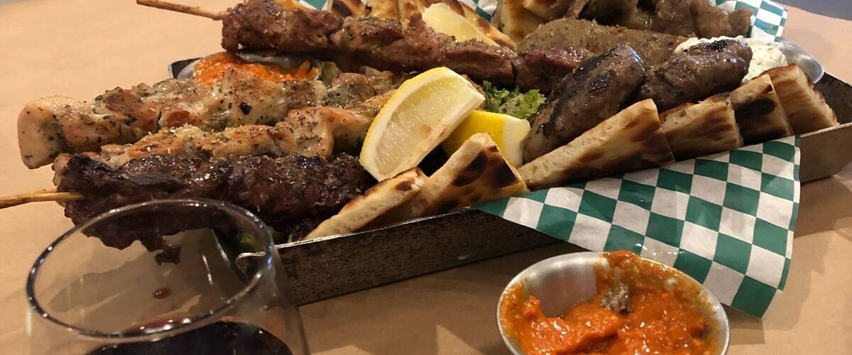 A variety of grilled meats and flatbreads on a table with a glass of red wine and a small bowl of sauce.