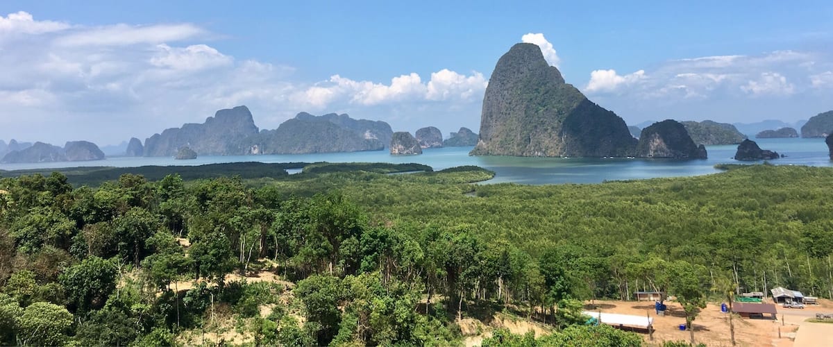 A coastal landscape with a prominent limestone peak, dense forest, and calm blue waters.
