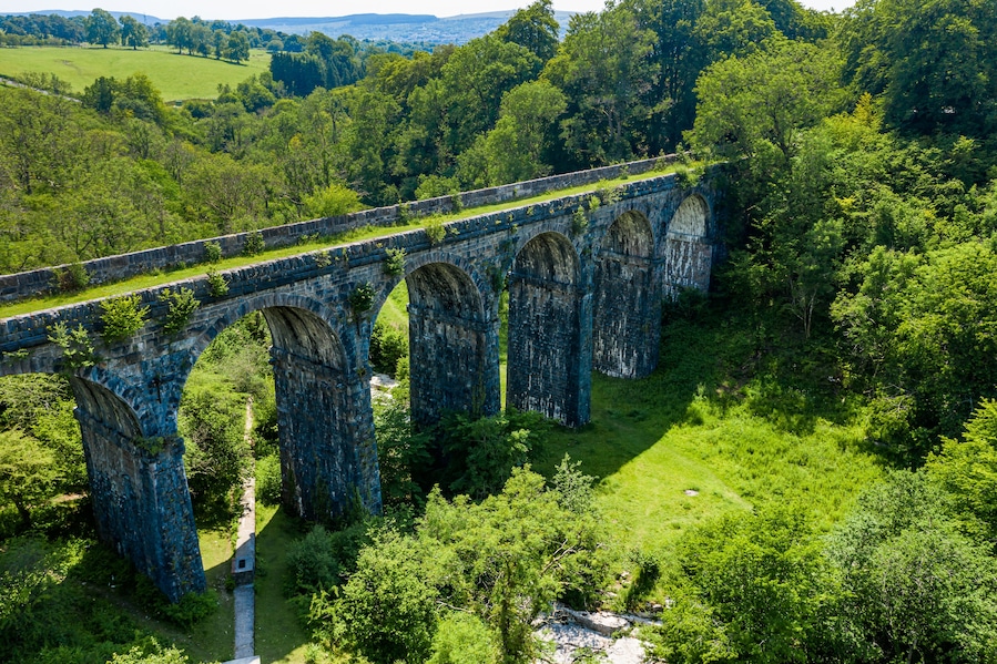 A stone viaduct over a river, surrounded by lush greenery and hills.
