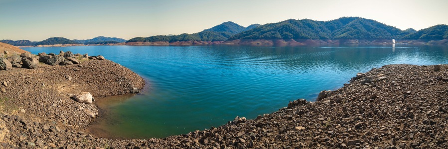 Shasta Lake at low water level with the gravel lake bed exposed in the Sacramento River, Northern California, United States, panoramic landscape with curving water’s edge