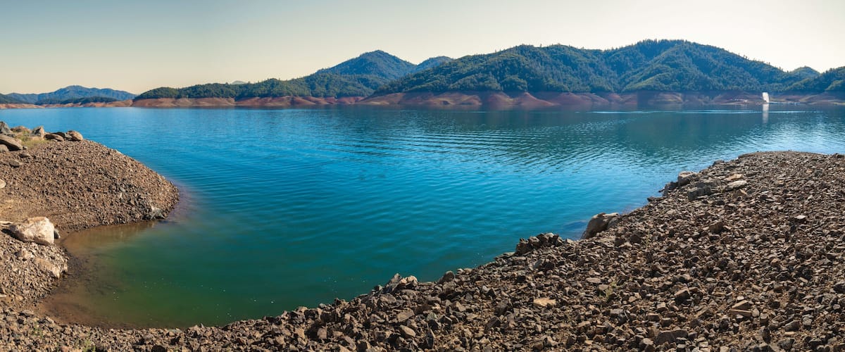 A calm lake with rocky shores and mountains in the background.