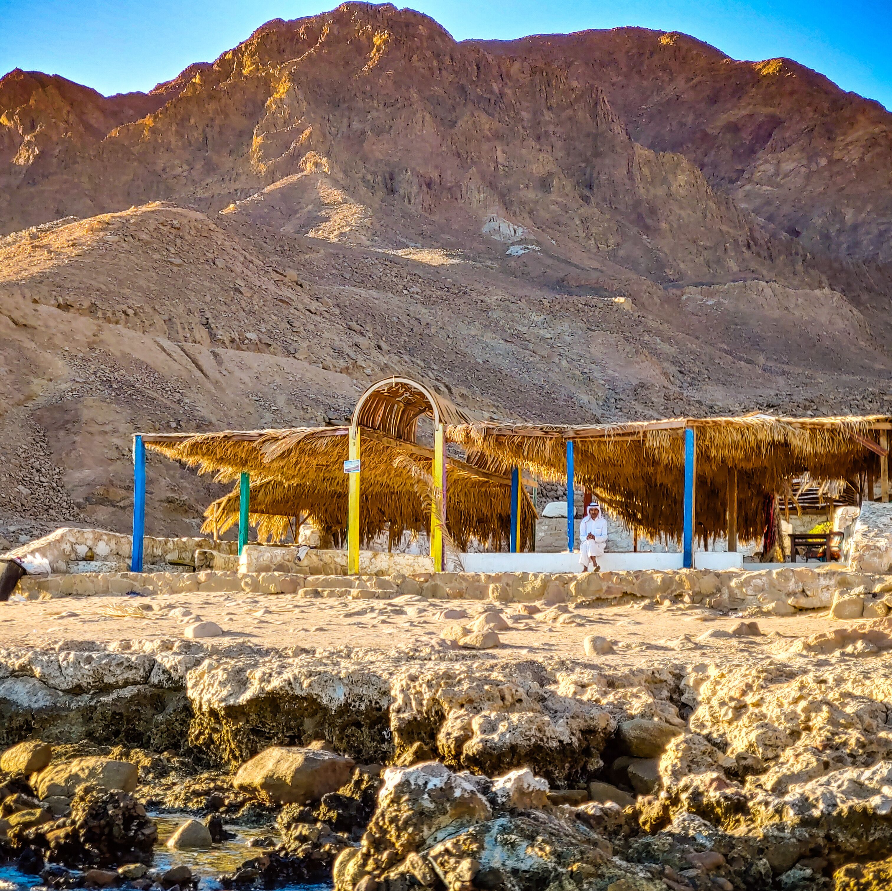 A traditional thatched-roof structure with a stone wall and a mountain in the background.