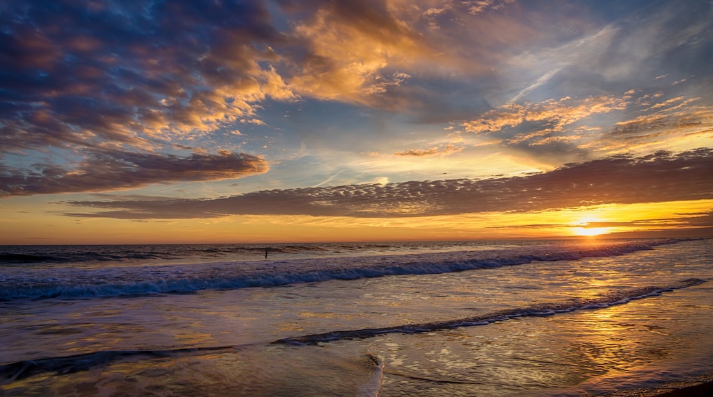 Een zonsondergang boven de oceaan met golven en een bewolkte lucht.