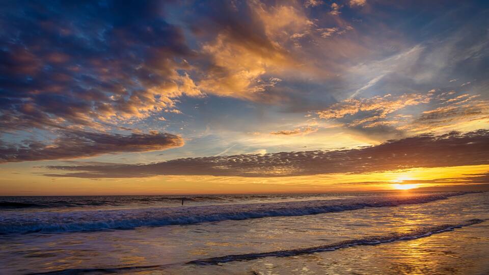 A sunset over the ocean with waves and a cloudy sky.
