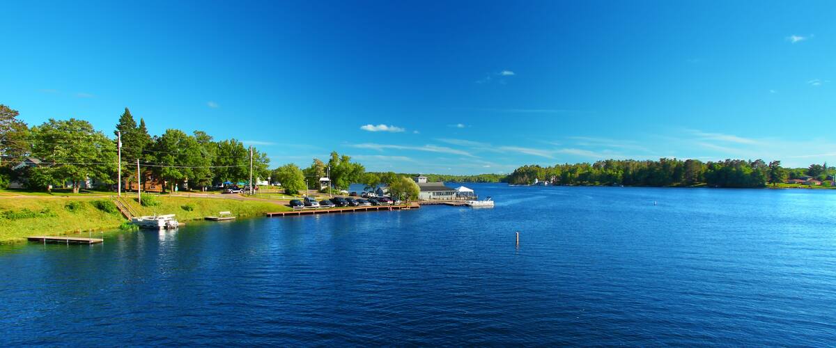 A calm lake with a dock, boats, and a small building.