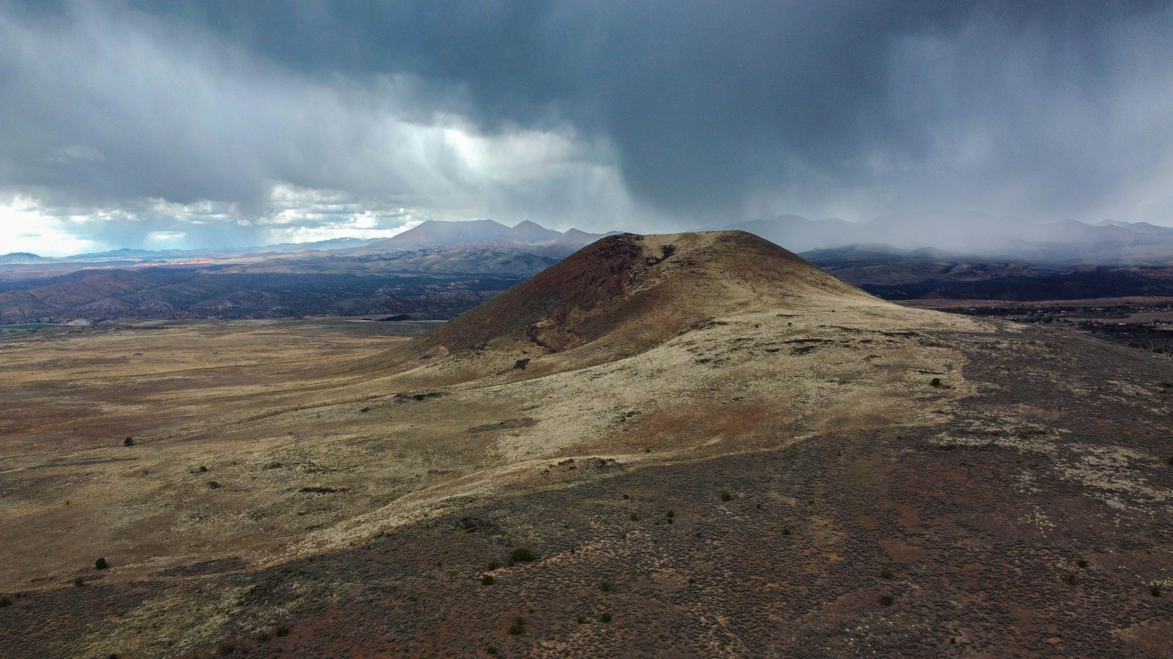 A barren hill with a flat top, surrounded by a vast, open landscape and distant mountains under a cloudy sky.