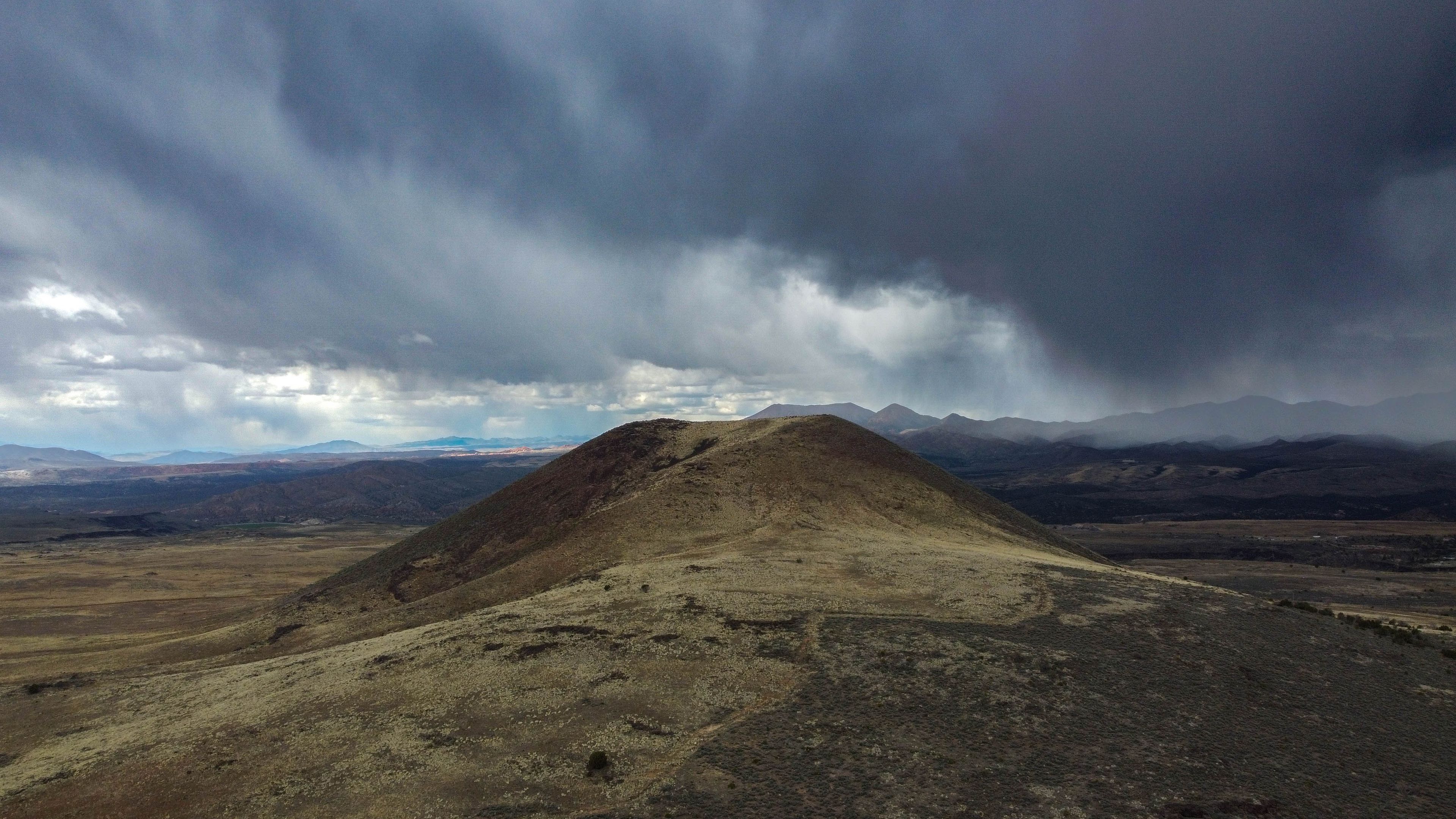 A barren hill with a mountain range in the background under a cloudy sky.