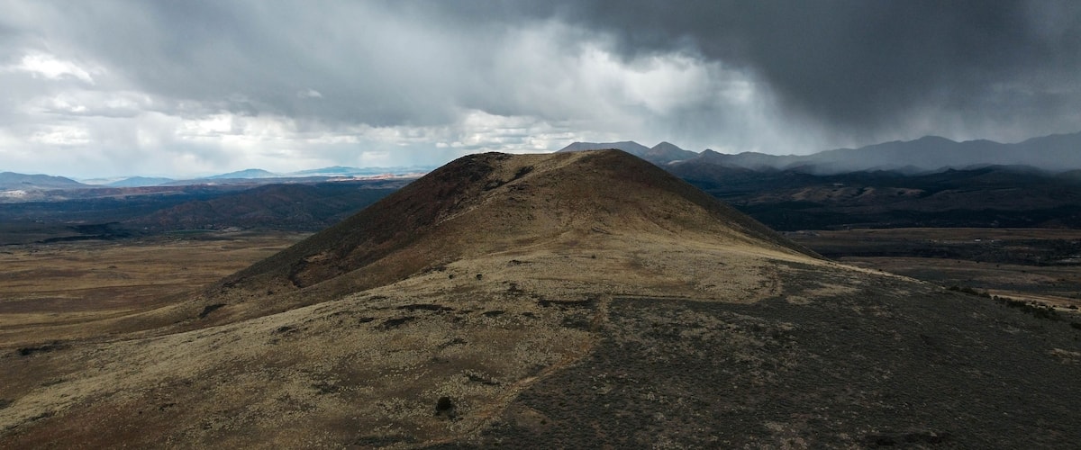 Una colina yerma con una cadena montañosa al fondo bajo un cielo nublado.