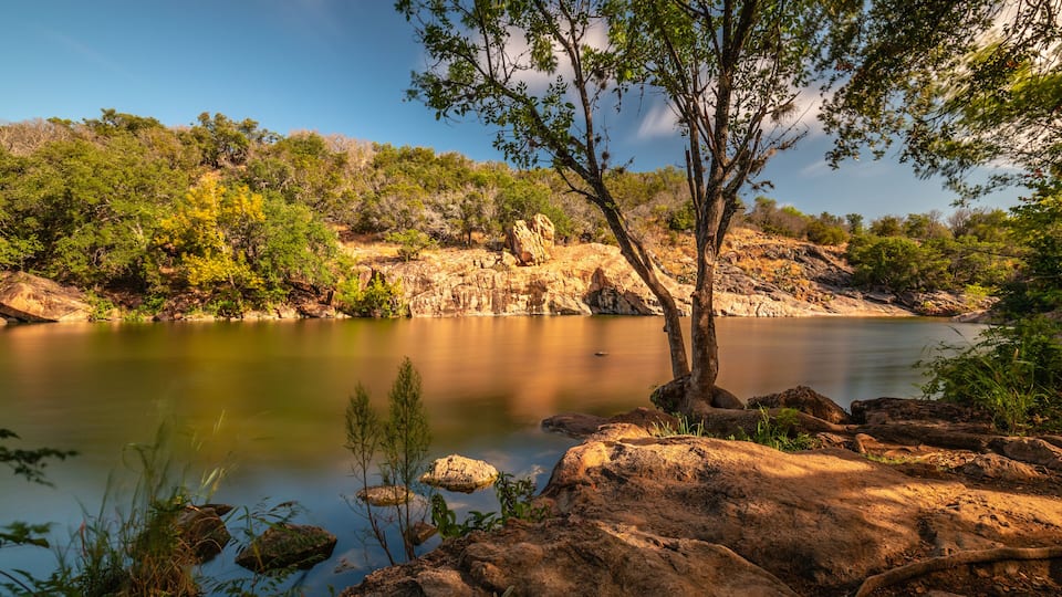 A calm river surrounded by rocky terrain and green vegetation.