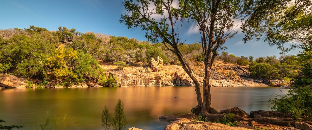 A calm river surrounded by rocky terrain and green vegetation.