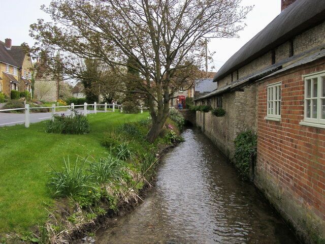 A narrow waterway flanked by brick buildings and a white fence.