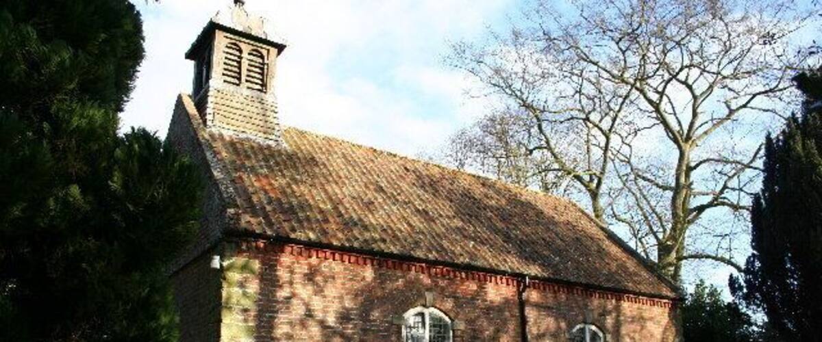 A small brick church with a steeple and two arched windows.