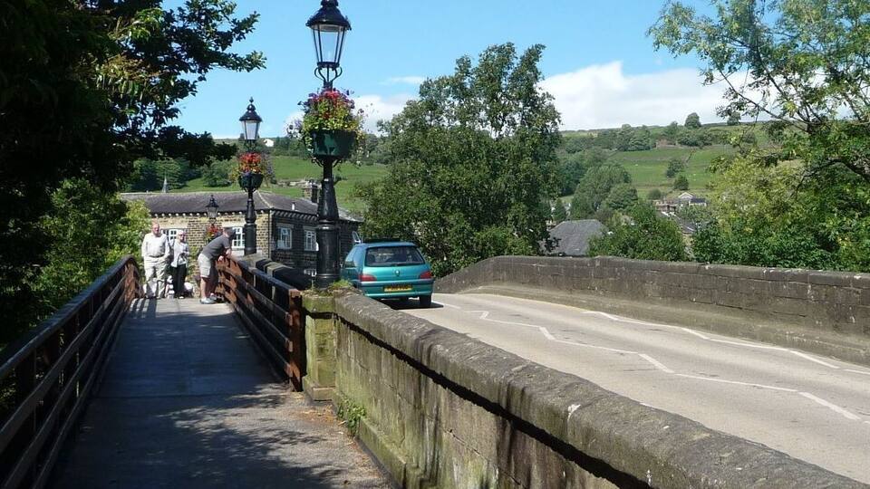 A stone bridge with a metal railing, a blue car, and a pedestrian walkway.