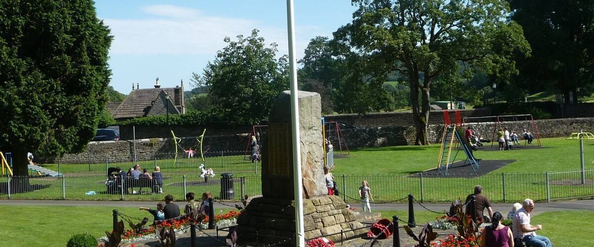 A park with a flagpole, playground, and flower beds.