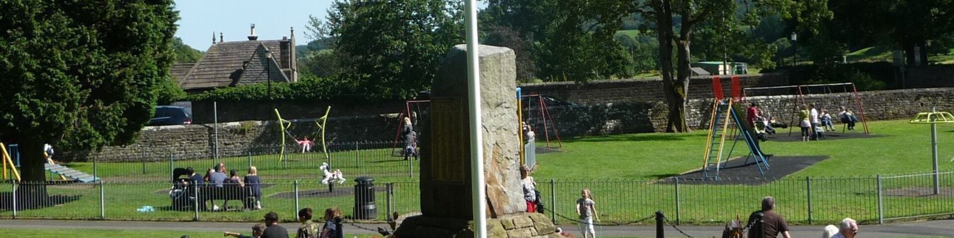 A park with a flagpole, playground, and flower beds.