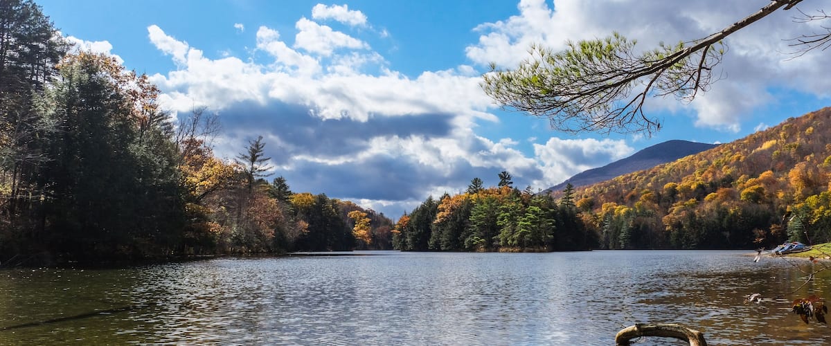 A calm lake surrounded by autumn-colored trees and a clear sky.