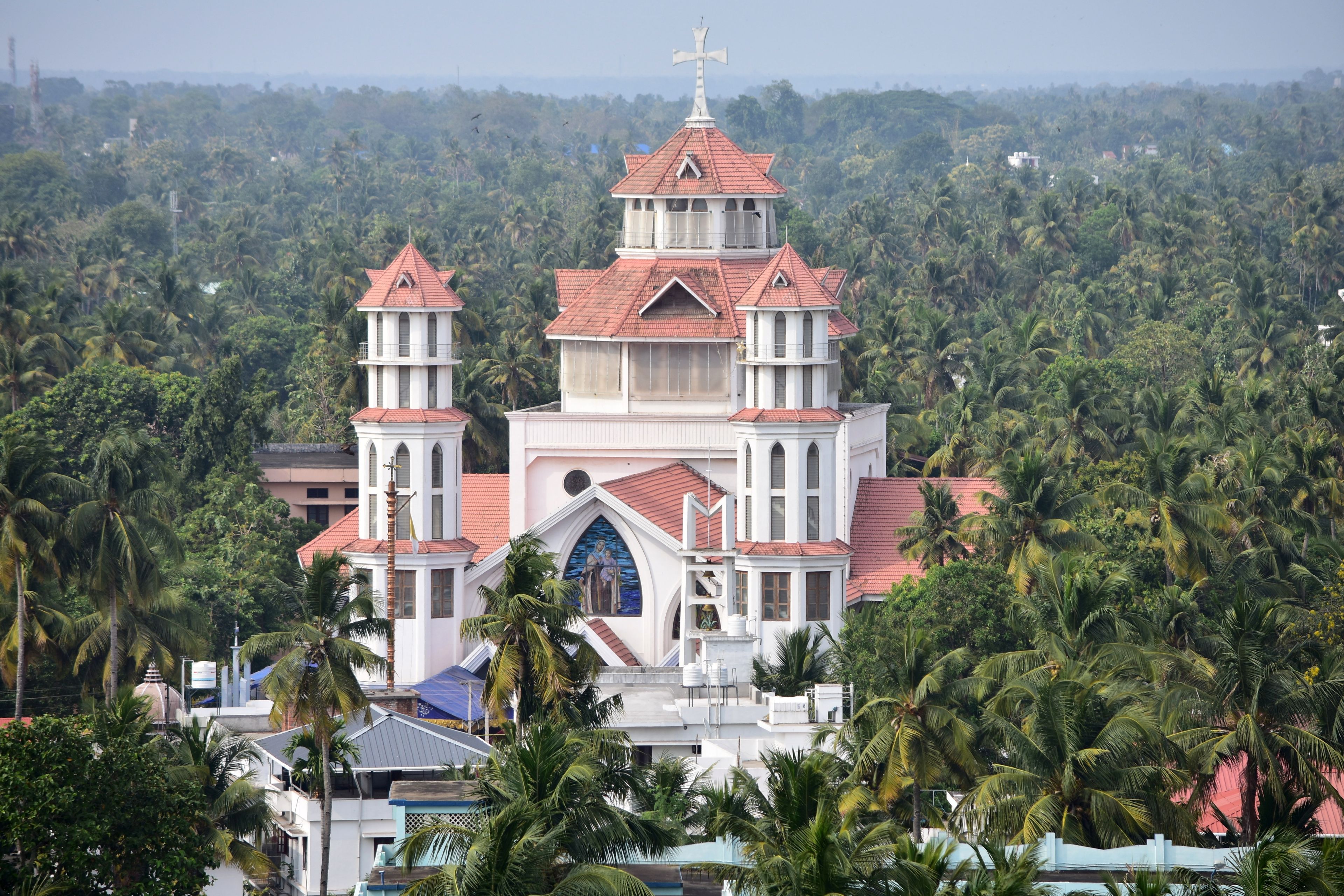 Una iglesia de techo rojo y paredes blancas, rodeada de palmeras frondosas.