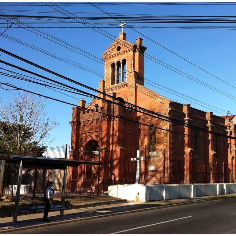 A red brick church with a bell tower and a bus stop in front.
