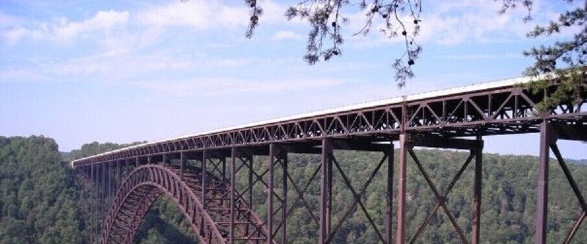 A large steel bridge spanning a deep gorge with dense forested hills in the background.