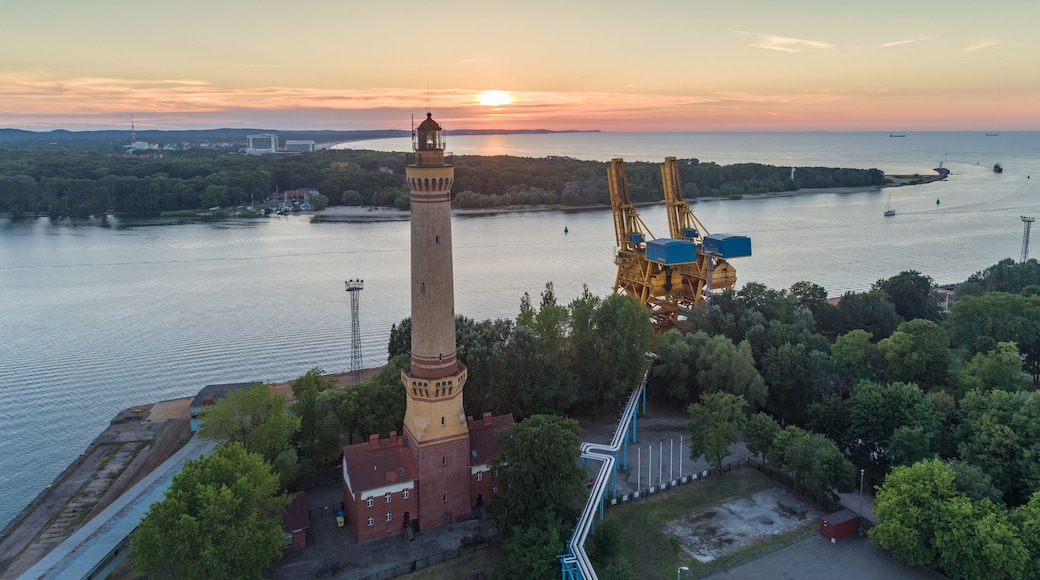Eine Küstenlandschaft mit einem markanten Leuchtturm, einem Kran und einem Sonnenuntergang über dem Wasser.