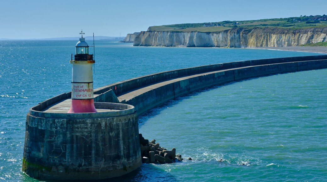 A lighthouse at Port of Newhaven, a coastal cliff, and a calm sea.