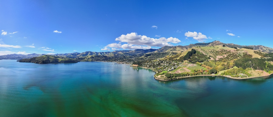 Un paisaje costero con un lago azul cristalino, colinas verdes y una pequeña isla con edificios.