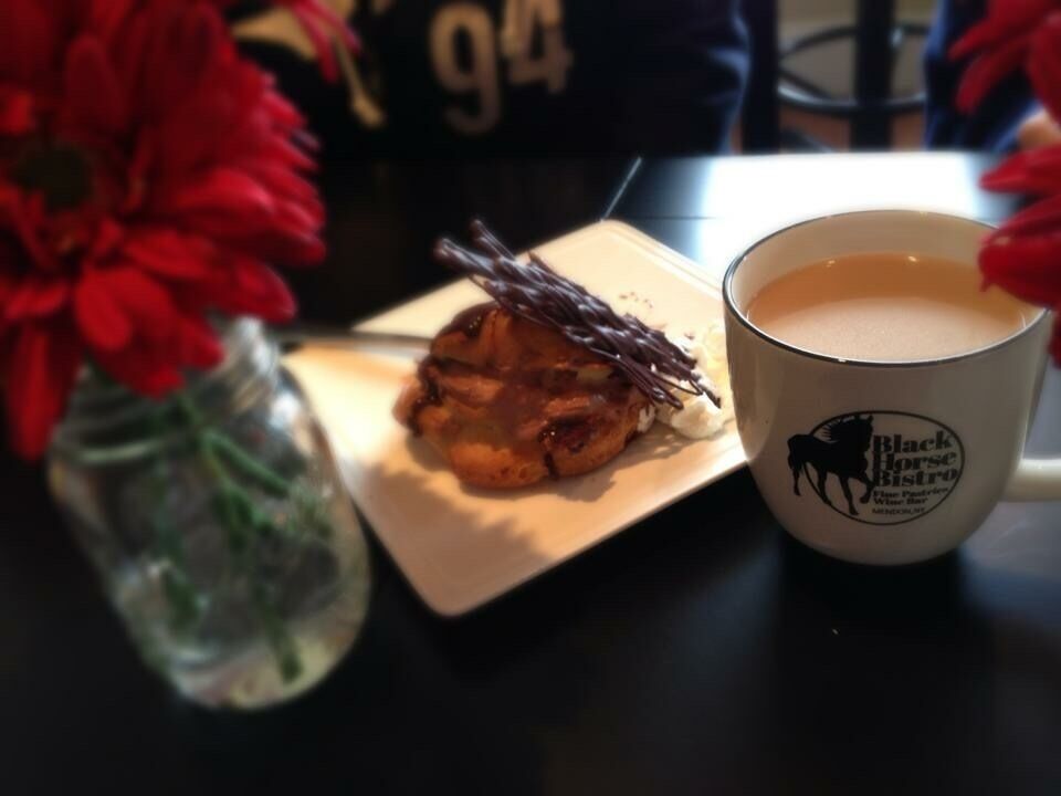 A mug with a horse logo, a plate with a pastry, and a vase with red flowers.