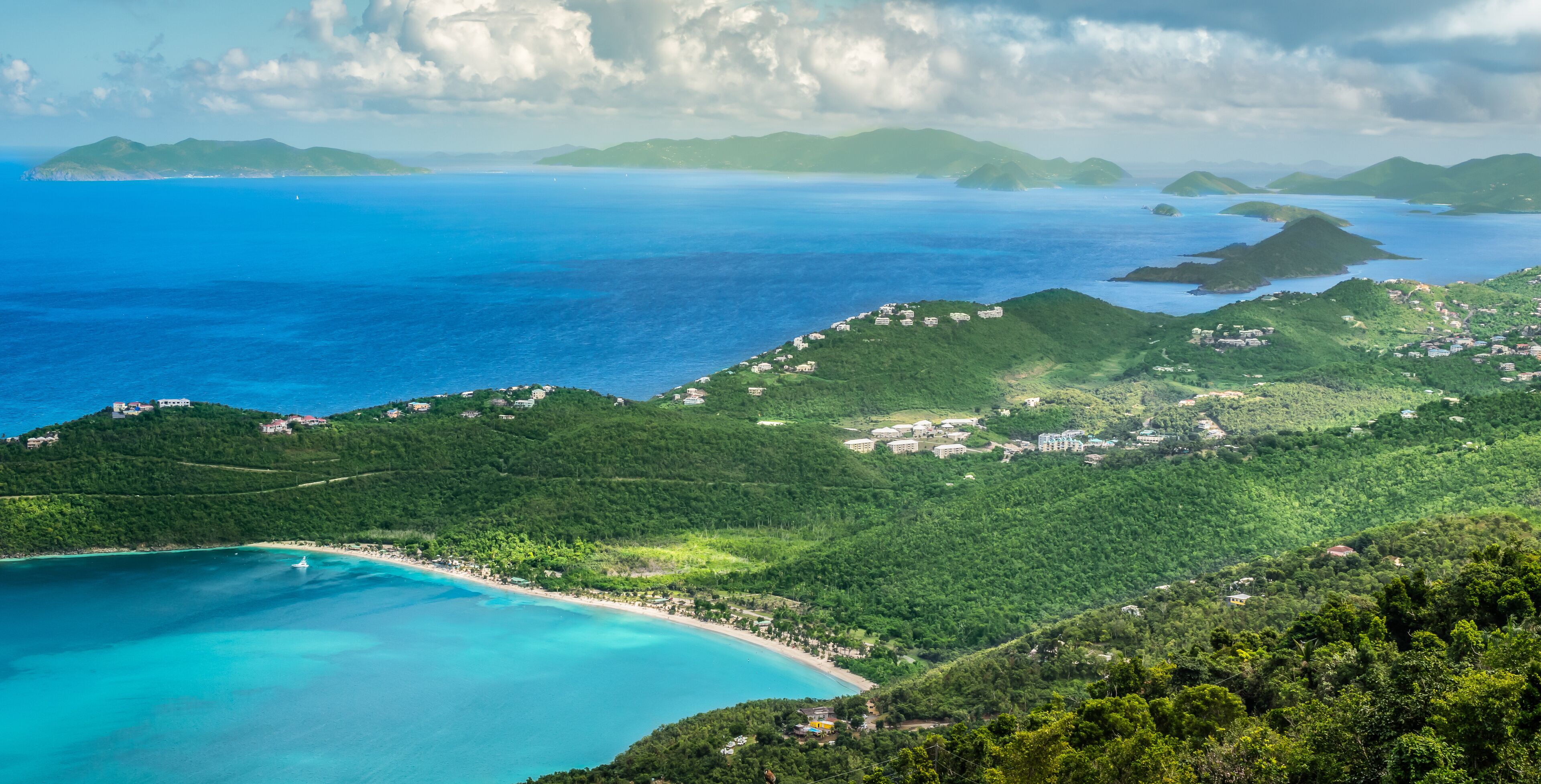 A coastal landscape with a beach, lush green hills, and a clear blue sea.
