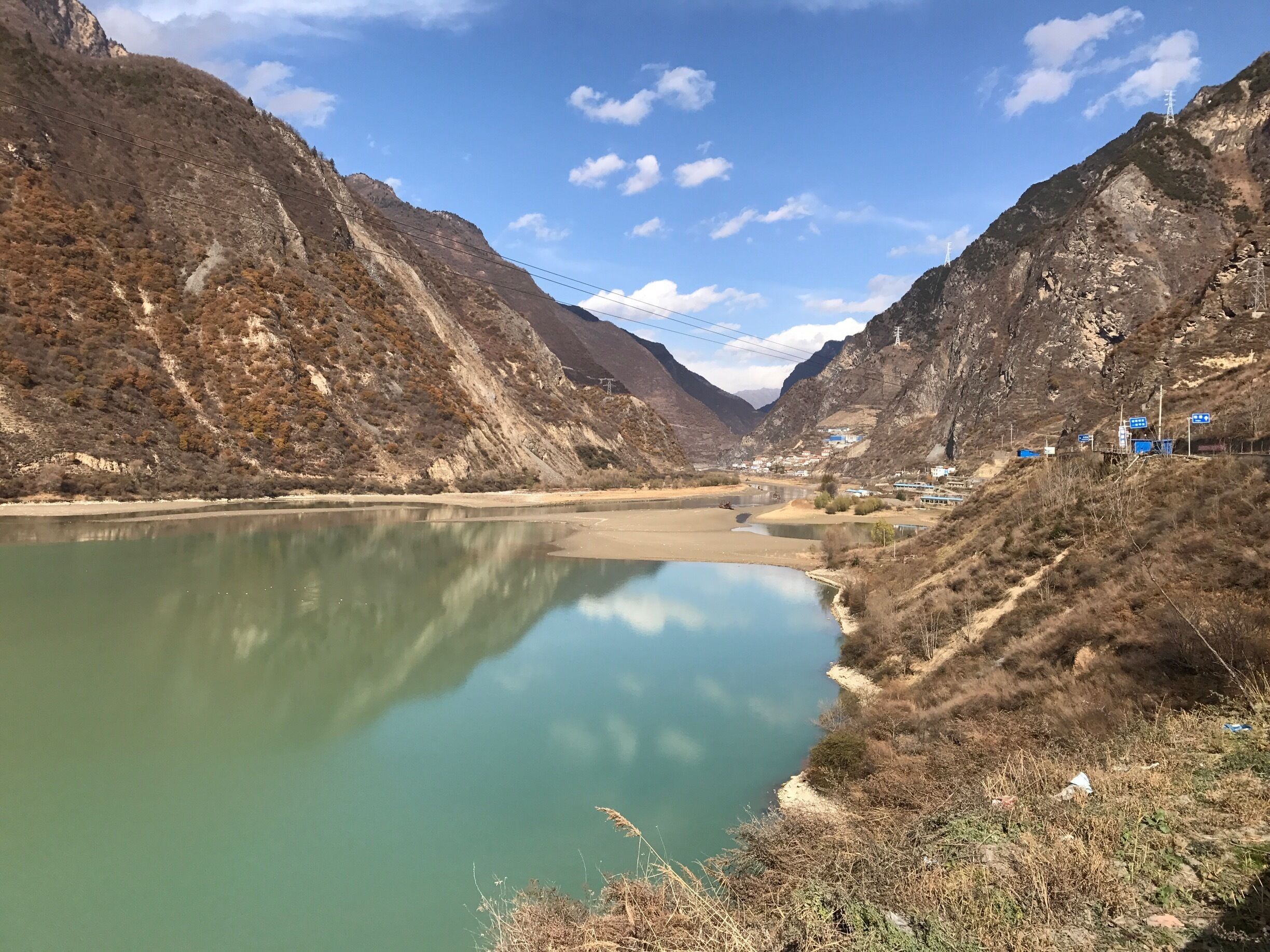 A river winding through a mountainous valley with sparse vegetation and a small settlement in the distance.