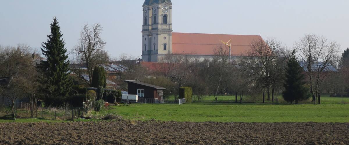 A church with a clock tower and a red-roofed building in a rural setting.