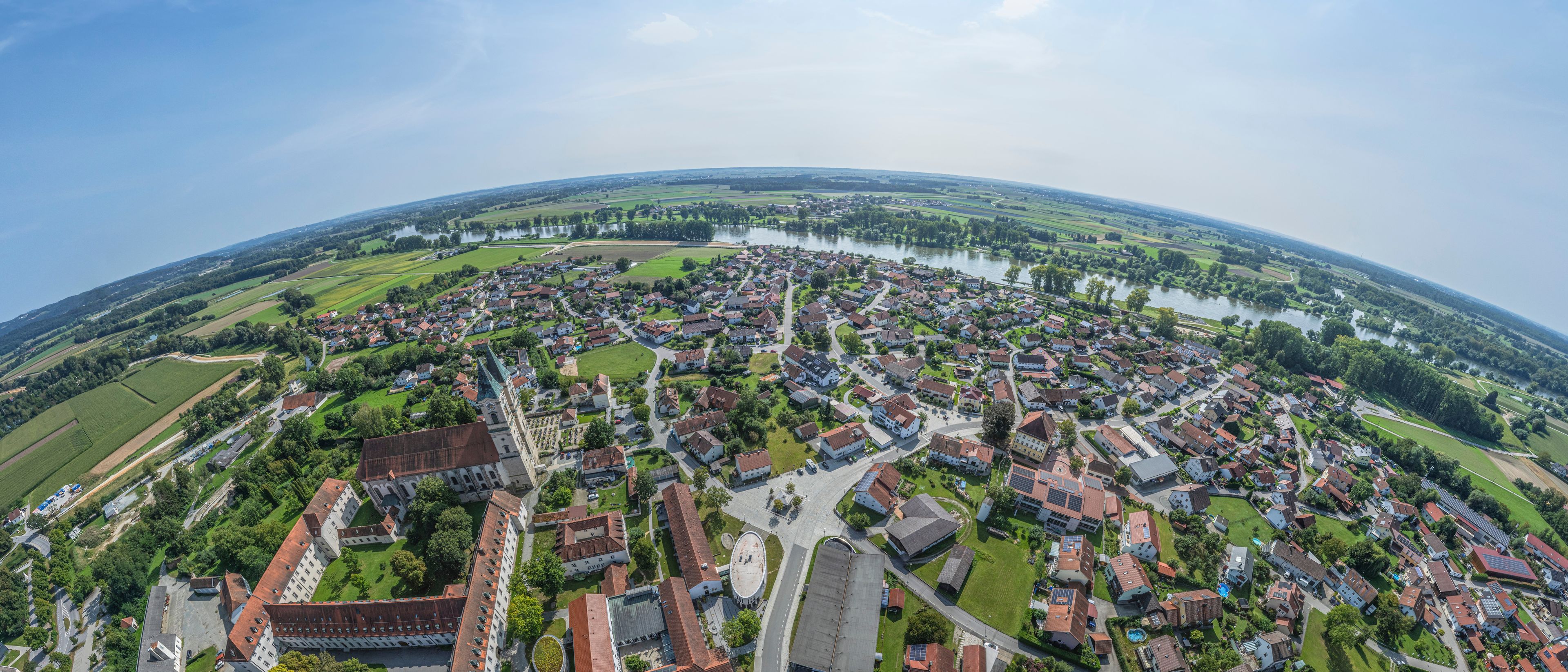 A panoramic view of a town with a river, green fields, and a prominent church.