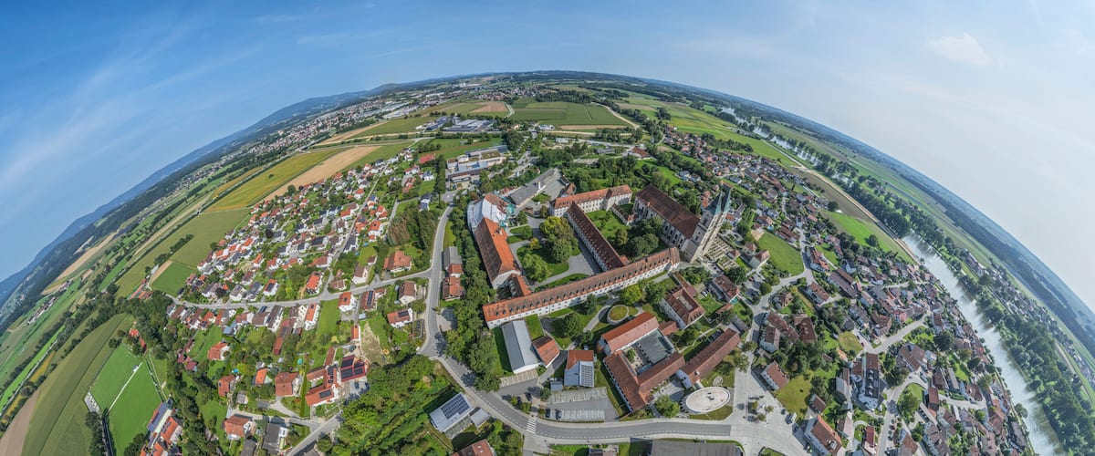 Ein weiter Blick auf eine Stadt mit einem Fluss, grünen Feldern und einer markanten Kirche.