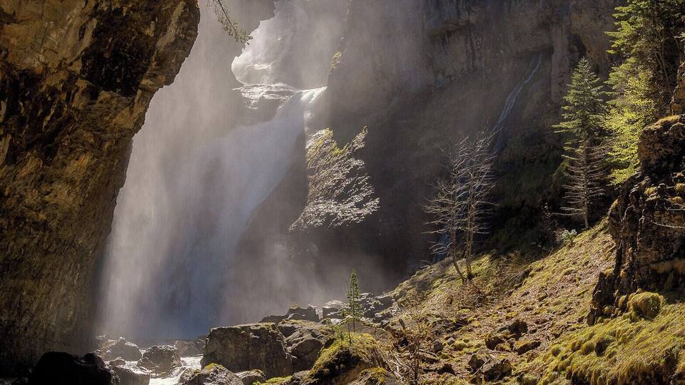 A waterfall cascading down a rocky cliff surrounded by trees and a flowing river at the base.